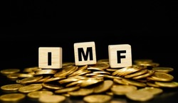 Stacks of gold coins with the letters IMF (International Monetary Fund) on a wooden cube. Business concept.                         