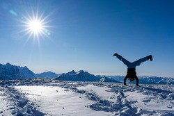Handstand straddle on snow caped mountain peak with blue sky and bright sunbeams.