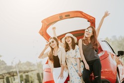 Three happy Asian girl best friends traveler celebrating a good time with arm up while sitting in car trunk 