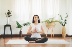 Shot of attractive healthy Asian woman doing yoga meditation at home in living room