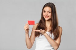 Smiling woman showing blank credit card in white t-shirt, isolated over gray background