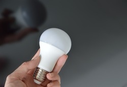 Hand holding a led lightbulb with reflection in black glass background