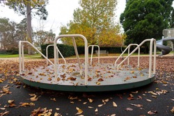 Empty playground roundabout surrounded by fallen autumn leaves in park.