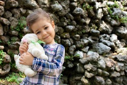 Portrait of cute little girl with lamb toy outside in park celebrating sacrifice feast. Beautiful child during Kurban Bayramı. Happy Eid al-Adha after covid-19 quarantine and lockdown.