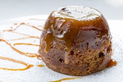 Sticky toffee pudding close up on a white sugar dusted plate drizzled with caramel sauce