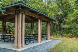 Empty small picnic pavilion with several tables on a cement pad with a grill alongside in the woodlands at the park