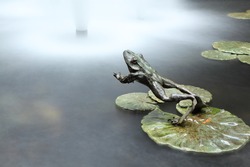 A frog jumps into water. A metal jumping frog sculpture. Long exposure.