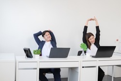 Young Asian businessman and businesswoman relaxing stretching arms, head and hands after work with laptop for a long time at office. Business people wear formal suit stretch oneself on break time