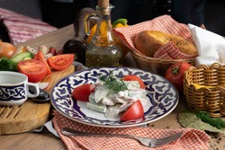 Vegetarian vegetable salad of radishes, cucumbers and tomatoes seasoned with sour cream in a plate with a traditional Uzbek pattern
