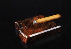 A lit cigar in an ashtray under dark lighting. Close-up