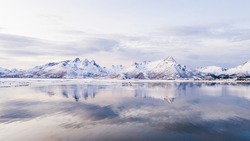 Breathtaking bird's eye view of high mountain rocky peaks covered with white snow reflected in Norway sea water. Breathtaking panoramic fjords landscape of Lofoten in winter, calm beauty of nature 