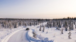 Bird’s eye view of vehicle car moving on rural road having good insurance for winter weather, aerial view of suv automobile driving in scenery area surrounded by coniferous forest