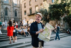Happy Caucasian man 60s enjoying solo trip vacations for exploring Italy during retirement, cheerful male tourist in straw hat using paper orientation map for walking around historis center