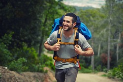 Attractive hiker with big traveling rucksack moving up on the mountain trail and smiling, happy traveler overcome big way smiling looking away, adventure travel and discovery