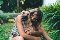Young woman hugging her dog in yard of resort hotel. Tourism, vacation and weekend. Owner and pet relationship and friendship. Attractive caucasian girl wear dress. Idyllic and tranquil lifestyle