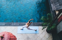 Flexible woman practice balance asana raising hands breathing at pool terrace, top view on fit girl doing stretching exercises during morning workout for feeling vitality and keeping healthy lifestyle