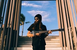 Young long haired hippie in sunglasses performing sounds music on ukulele equipment enjoying rock'n'roll pastime, talented hipster guy playing solo heavy metal while creating melody art on leisure