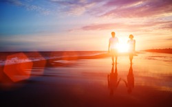 Honeymoon romantic couple in love walking on the beach on orange sunset background, happy young couple embracing enjoying ocean sunset during travel holidays vacation