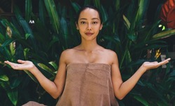 Portrait of attractive Asian woman in towel raising hands and looking at camera while waiting for spa procedure at nature, charming Korean female posing as beauty model during weekend leisure