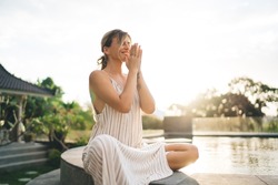 Young pleased woman practicing yoga and meditating on swimming pool edge in yard of resort hotel. Tourism, vacation and weekend. European girl. Sunset. Idyllic and tranquility lifestyle on Bali island