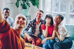 Happy multiracial friends posing for making selfie content during gather meeting for gambling and wagering with cards and poker chips, cheerful hipster guys enjoying together recreation in home flat