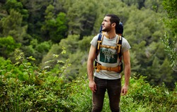 Young hiker with backpack look around while planning mountain walk trip, man hiker get lost in beautiful green forest and looking to laterally copy space area for your text message or information