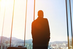 Silhouette of man managing director is examining the challenges the company after the refusal of investors in financing, while standing in evening time against office window background with copy space