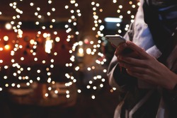 Cropped image of person booking hotel via smart phone application during vacation holidays in Christmas. Closely of a hipster girl is using her cell telephone, while is standing outdoors in night time