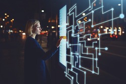 Young woman touching sensitive screen while selecting surface option. Female standing at big display with advanced innovative device with infographics design elements.Person with futuristic technology