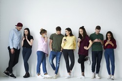 Full length portrait of group of diverse people use smartphones against copy space background with area for your advertising. Young friends in casual wear holding cellphones  using popular application