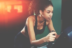 Attractive young woman at the gym riding on spinning bike. Confident afro American woman cycling on gym machine bicycle. Motivation and sporty goal concept