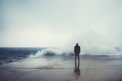 Feeling of freedom, back view of adult man standing on pier facing to the sea with big waves beats against the shore on a cloudy autumn day, alone depress person,the power of nature, storm on seashore