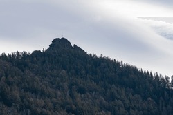 Stone rock on top of a mountain among a pine forest. A graceful mountain against a cloudy sky.