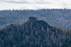 Stone rock on top of a mountain among a pine forest. A graceful mountain against a cloudy sky.