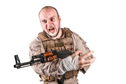Angry soldier with grimace of hatred aiming in front of him ready to open fire at any moment. He wears desert combat uniform and military grade bulletproof vest. He shouts. Isolated, white background.