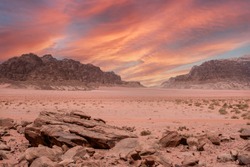 Fantastic view of the endless arid valley, Wadi Rum desert, Jordania. Spectacular sky with large red dramatic clouds, mountain range, lots of red sand and a few bushes and rocks in the background.