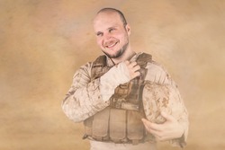 Wounded marine standing in the middle of desert during sandstorm. He is looking into camera and smile. Soldier wears combat bulletproof vest, special uniform with some extra gear. Abstract background.