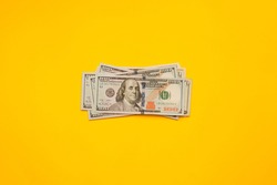 Several US dollars banknotes lies on a yellow background. One hundred dollars on top. View from above.