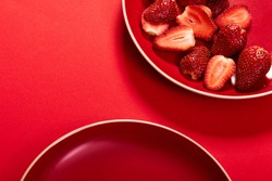 top view of a monochromatic composition or flat lay with sliced strawberries served on a ceramic plate on red background