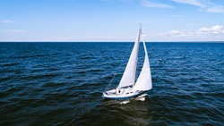 Aerial photography of yacht with white sails in dark blue open space. The good wind fills sails on a sunny summer day. 
