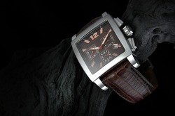 luxury watch on black wood with black background. The watch is made of precious metal and a crocodile strap. Commercial and product photo. A beautifully lit elegant men's watch. 
