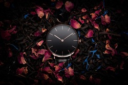 A luxury gold watch with a black dial. A watch on a beautiful stand, on a beautiful background of dried flowers, dried rose, colorful flowers. Woman / Man fashion
