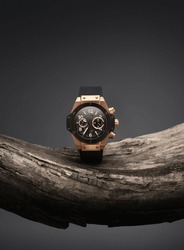 Beautiful gold men's watch with a black strap on a wooden stand, on a gray background. Beautiful gold watch. A luxury brand watch. 