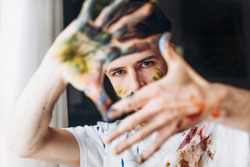 The artist creates a frame with his hands soiled with watercolor paints. Portrait of a young creative artist, the process of creating a picture.