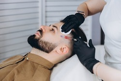 Stylish bearded man visiting aesthetic clinic, getting lips filler, closeup. Attractive Man having beauty injection at male spa salon background. Anti-aging treatment for men concept 