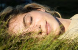 close-up of a beautiful teenage girl lying on green grass over sunlight. Eyes closed, enjoying nature outdoors. Cute teenage girl relaxing daydreaming in the park. Spring, summer, sunbathing