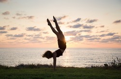 young slender woman does handstand at sunset on sea coast, beautiful silhouette. concept of cheerfulness, sports education, healthy lifestyle. girl trains with pleasure. soft focus, photo in motion
