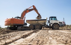 gray articulated dump truck and crawler excavator at a construction site during loading of soil. earthworks at the construction site
