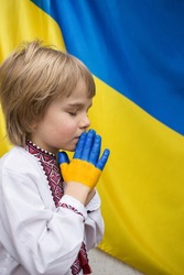 Children against war. Russia's invasion of Ukraine, request for world community's help. A child against background of Ukrainian flag with hands painted in yellow and blue, gesture of faith and hope