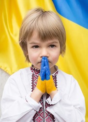 child's hands are painted in colors of Ukrainian flag. boy in national clothes asks for help. children's prayer to stop war in Ukraine. Prayer, Faith, Hope. asking for help from world community